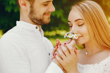 Fototapeta premium A beautiful and gentle girl with light hair and a white dress is walking in a sunny summer forest with her handsome guy in a white shirt and dark pants