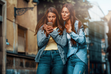 Two young women using smartphone in the street and look very surprised of what they see