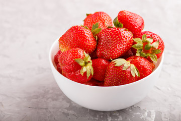 Fresh red strawberry in white bowl on gray concrete background. side view.
