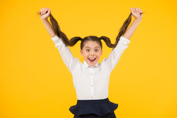 Easy hair for school. Happy small girl holding long brunette hair on yellow background. Styling hair for school in beauty salon. Her hair is her inspiration