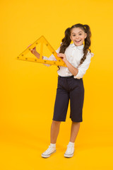 Learning by doing. Cute small girl learning shapes at geometry lesson on yellow background. Adorable little child holding triangle, learning tool. Self learning and education