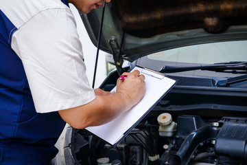 The car mechanic is recording the checklist of the car's bad condition.