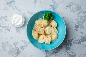 Dumplings with sour cream and herbs on grey concrete table