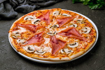 Pizza with ham and mushrooms on black concrete table