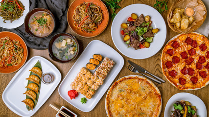 assorted food set on table top view. beef wok noodles, miso soup, gedza, japan rolls, sushi, pizza pepperoni, pizza quatro formaggi.