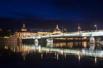 Fototapeta premium Pont de la Guillotiere bridge in Lyon, France over a panorama of the riverbank of the Rhone river (Quais de Rhone) at night with the main monuments of the old Lyon in background