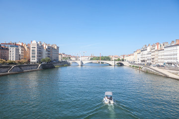 Fototapeta na wymiar Boat approaching Pont Bonaparte bridge of Saone river near the Quais de Saone riverbank and riverside in the city center of Lyon during a summer afternoon