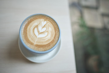 Hot cappuccino coffee cup with tree shape latte art milk foam on wood table near window in garden at cafe restaurant