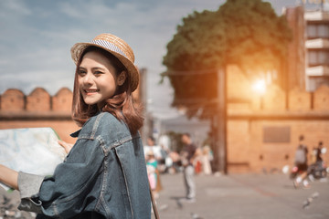 Smiling woman traveler in thapae gate landmark chiangmai thailand with backpack holding world map on holiday, relaxation concept, travel concept