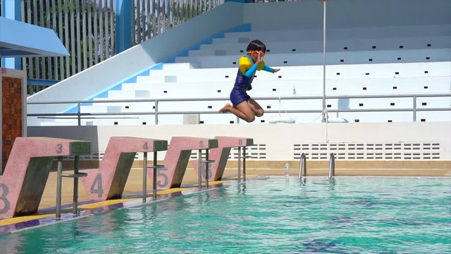A cheery view of a boy in long shorts jumping in the cyan-blue water of the spacious swimming pool in summer in slow motion