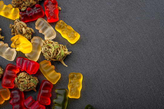 Cannabis edibles, medical marijuana, CBD infused gummies and edible pot concept theme with close up on colorful gummy bears and weed buds on dark background with copy space