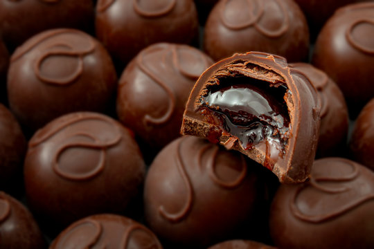 Sweet confectionery and candy indulgence concept theme with close up on a bitten cherry filled chocolate praline on top of many other delicious pralines with copy space