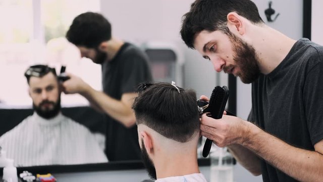 attractive businessman sitting in a chair while getting a modern and stylish haircut from a barber at the hair salon