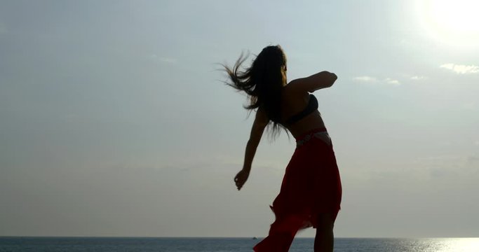slender sexy woman is dancing against seascape, sun and skyline, silhouette view