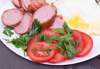 Fototapeta na wymiar Breakfast, fried egg, sausage, salad, tomato and greens on a plate.