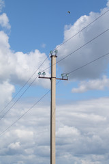 Fototapeta na wymiar Concrete electric pole with wires in a green field against a blue sky.