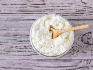 Wooden spoon in a jar with fresh cottage cheese on a rustic pink table. The view from the top.