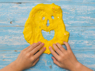 The child makes a funny face of yellow slime on a wooden table.