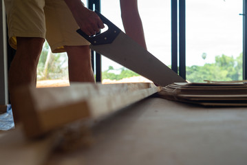 Closeup hand of man holds the manual saw and cuts the wooden in the house under construction