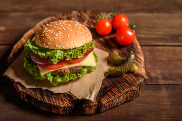 Tasty grilled homemade burger with beef, tomato, cheese, cucumber and lettuce. Delicious grilled burgers. Craft beef burger and french fries on wooden table.