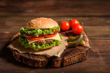 Tasty grilled homemade burger with beef, tomato, cheese, cucumber and lettuce. Delicious grilled burgers. Craft beef burger and french fries on wooden table.