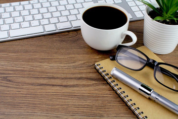 ffice desk wooden table with computer,keyboard,pen,notebook,glasses and cup of coffee