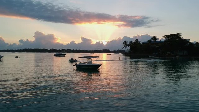 A drone shot at low altitude moving towards a small boat, while another tiny ouboard pass trough the scene, at sunrise in a small pier in a paradise island