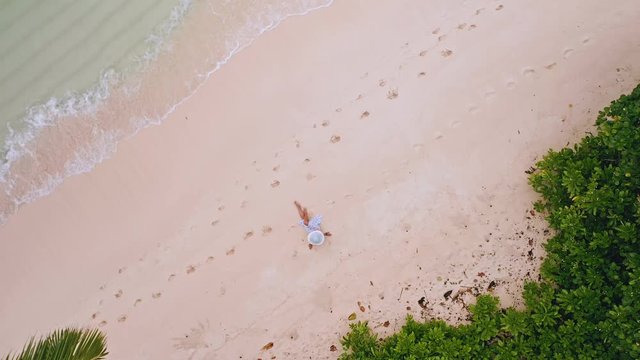 4k aerial view vertical circle move up footage from girl sitting on a white sand beach surrounded by crystal clear turquoise shallow ocean and pam trees on tropical island