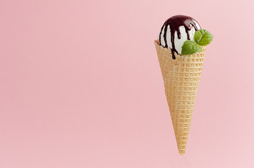 White creamy ice cream in crisp waffle cone with chocolate sauce, mint leaf on pastel pink background, copy space.