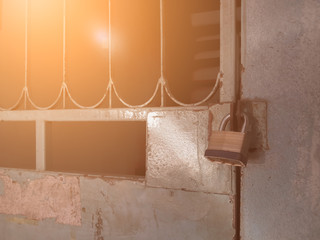 Brass steel padlock was locked with closed strong old weathered gray coloring wrought iron door with orange flare radial sun lighting background.
