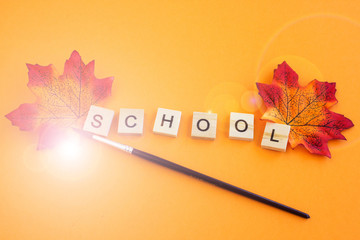 Colorful autumn school background. The inscription "school" in wooden letters on an orange background. The concept of the beginning of the school year. Place for text.