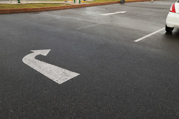 Closeup of arrow sign on asphalt ground of the parking lot after raining. 