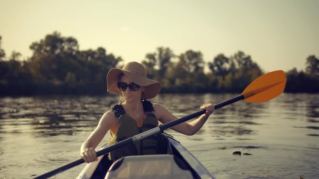 Girl Traveller In Life Vest Swims In Kayak Boat In Tranquil Pond.Girl In Kayak.Woman Exploring Calm River By Canoe.Pretty Woman In Hat And Sunglasses Kayaking On Lake At Sunset And Holds Oar Close Up 