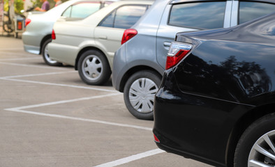 Closeup of rear side or back side of black car and other cars parking in outdoor parking area.