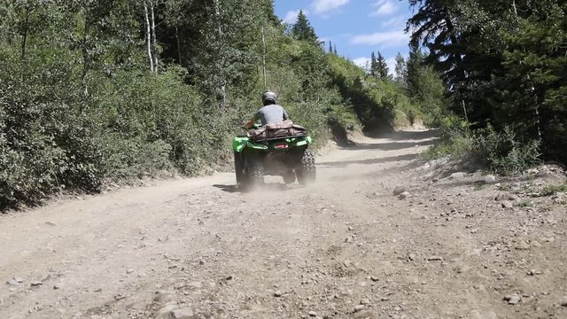 Slow motion shot of an ATV Rider driving his quad on a dirt path in the mountains, leaving a large dirt cloud behind him.