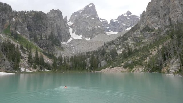 Man swimming in freezing cold water glacier fed lake in the Grand Tetons National Park 4k