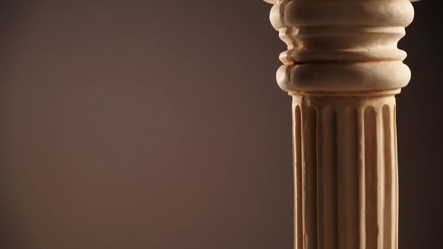 Single ancient greek column rotating slowly on brown color background, copy space text area