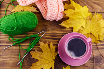 Cup of coffee, ball of yarn, knitting, knitted scarf and yellow maple leaves on wooden table. Autumn still life