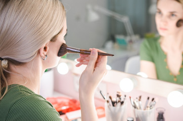 Young pretty woman making make-up near mirror in studio