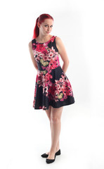 full length portrait of red haired girl wearing a cute flower patterned dress. Standing pose against a  white studio background.