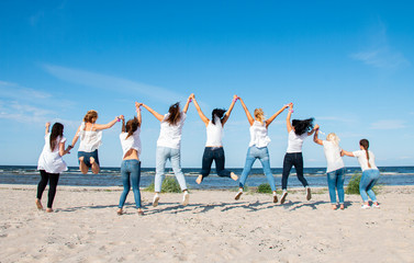 nine girls in white blouses jump to the top on the shores of the blue sea