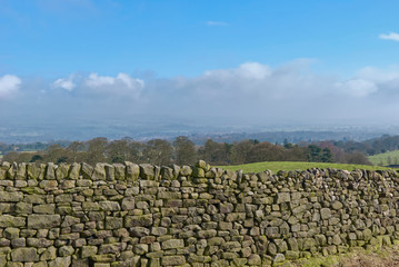 Fototapeta na wymiar Detail of a Yorkshire Drystone wall on the Fells at Ilkley Moor in West Yorkshire, England, on one bright January Morning, with haze in the distance.