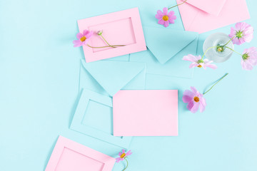 Flowers composition romantic. Pink cosmos flowers, pink and blue envelopes on pastel blue background. Flat lay, top view, copy space
