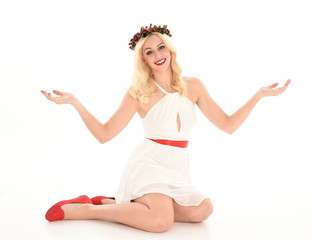 full length portrait of blonde girl wearing a white dress and flower crown.  Sitting pose, isolated against a  white studio background.
