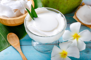 Young coconut pudding served in a glass cup decorated with coconut meat looks delicious on the banana leaves and a beautiful blue wooden table.