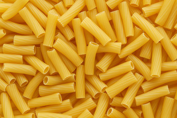 Dry uncooked tortiglioni or rigatoni pasta as a background.
