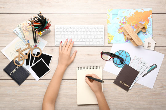 Hands of female travel blogger with computer keyboard, notebook, map and passport on wooden background