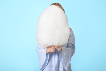Young woman with tasty cotton candy on color background