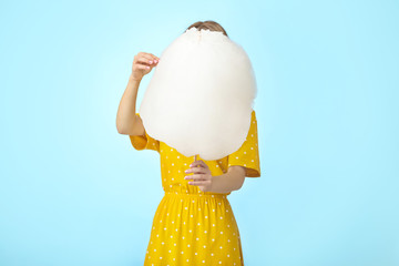 Young woman with tasty cotton candy on color background
