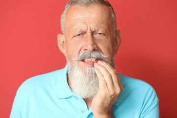 Senior man suffering from toothache against color background